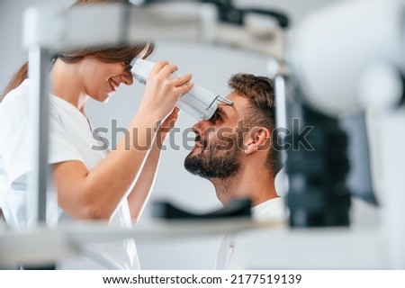 Side view. Man's vision checked by female doctor in the clinic by using special optometrist device. Royalty-Free Stock Photo #2177519139