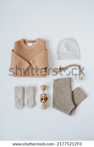 Stylish elegant newborn baby clothes, accessories and toys collage on white background. Peachy sweater, leggings, bib, pacifier, hat, socks. Neutral pastel beige color. Flat lay, top view