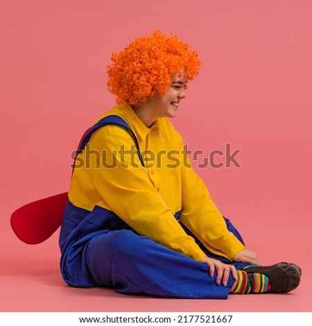 funny clown in a wig and a yellow-blue suit with a propeller on his back sits on a colored background