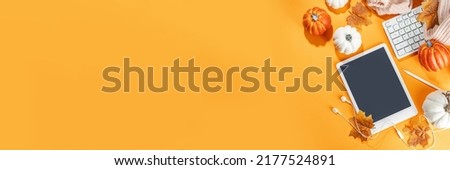 Cozy fall background with tablet, ear-pods, white, orange pumpkins, autumn leaves decor on high-colored orange background. Autumn still life composition. 
