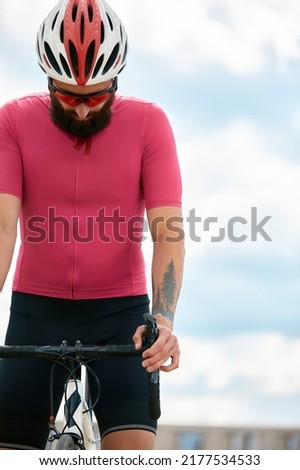 European bearded cyclist wearing helmet with pink t-shirt. Advise people to protection, blue sky on the background