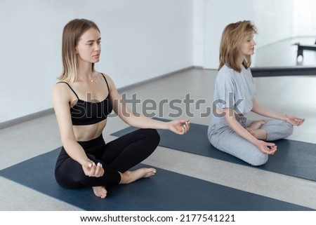 Two athletic attractive girls sit in lotus position on yoga mat indoors .Yoga, fitness and healthy lifestyle