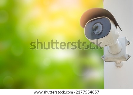 CCTV with water proof cover installed on wall in the blurred green tree background with orange sunlight. Digital security camera technology concept of surveillance monitoring for public safety. Royalty-Free Stock Photo #2177554857