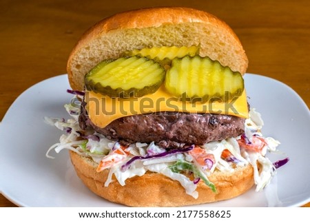 cheese burger resting on cole slaw and top with pickles on a brioche bun Royalty-Free Stock Photo #2177558625