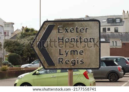 Dirty road sign by a car park in Sidmouth, Devon, pointing the way out of town to Exeter, Honiton and Lyme Regis