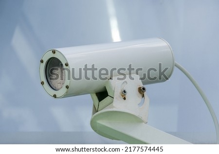 Outdoor mounted, white professional weatherproof surveillance camera against a blurred background, selective sharpness, lots of copy space