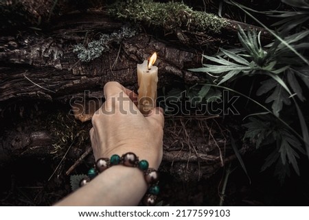 burning candles and a womans hand with a bracelet on a dark natural background. pagan wiccan, slavic traditions. Witchcraft, esoteric spiritual ritual for mabon, samhain.  Royalty-Free Stock Photo #2177599103