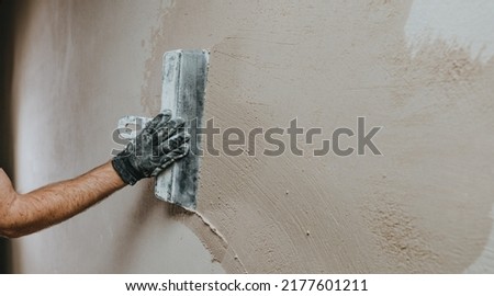Male builder in work overalls plastering a wall using a construction trowel. Horizontal panorama banner with blank space for text. Royalty-Free Stock Photo #2177601211