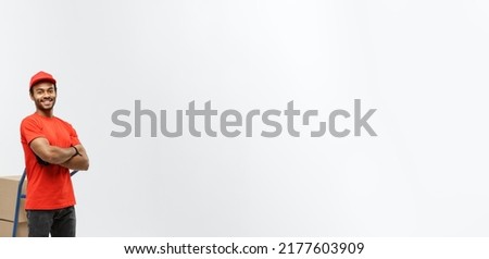Delivery Concept - Portrait of Handsome African American delivery man or courier pushing hand truck with stack of boxes. Isolated on Grey studio Background. Copy Space.