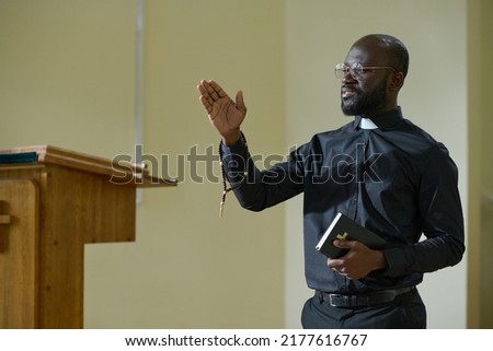 Confident African American man in pastor apparel with clerical collar preaching during church service in front of parishioners Royalty-Free Stock Photo #2177616767