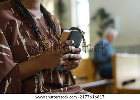 Hands of young black woman with Holy Bible and rosary beads with small wooden cross standing in church and praying after sermon Royalty-Free Stock Photo #2177616817