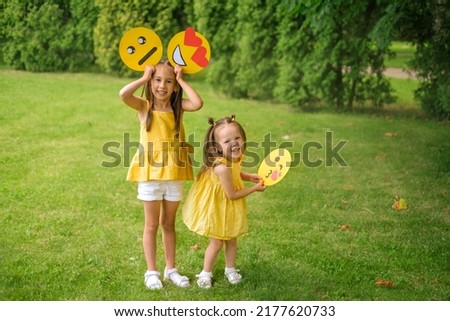 Kids have fun in nature in the park, holding paper emojis with different emotions on face