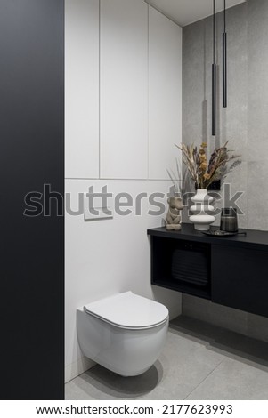 Stylish lavatory interior with white toilet, gray concrete style wall and floor tiles, modern lighting and decorations Royalty-Free Stock Photo #2177623993