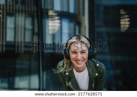 Happy blonde girl in headphones , leather jacket and white t-shirt laughing, enjoying music outdoors. Swedish young woman at weekend walking in the city. Happy people concept. Hipster student outdoors Royalty-Free Stock Photo #2177628571
