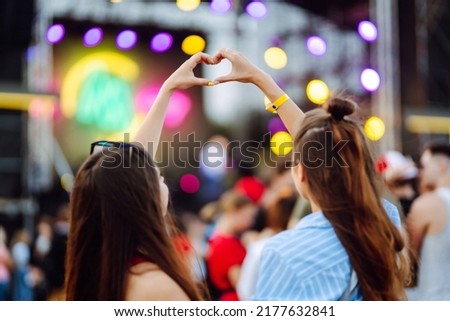 Heart shaped hands at concert, loving the artist and the festival. Music concert with lights and silhouette of people enjoying the concert. Royalty-Free Stock Photo #2177632841