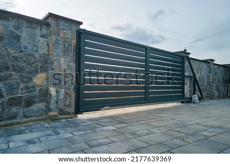 Wide automatic sliding gate with remote control installed in high stone fense wall. Security and protection concept Royalty-Free Stock Photo #2177639369