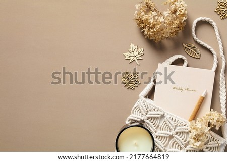 Stylish feminine desk table with macrame bag, dried flowers, candle, paper notebook, pen on brown background. Cozy home feminine workspace, boho style. Autumn, fall concept. Royalty-Free Stock Photo #2177664819