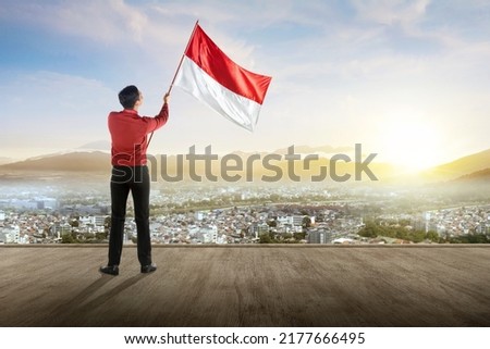 Rear view of Asian businessman holding an Indonesian flag with a blue sky background. Indonesian independence day