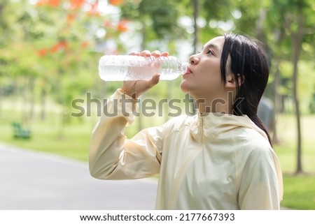 Beautiful young woman asina drinking water from bottle after running in park.