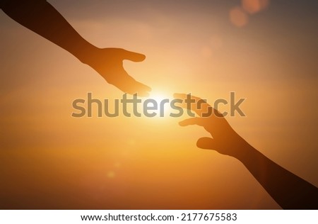 Silhouette of reaching, giving a helping hand, hope and support each other over sunset background.