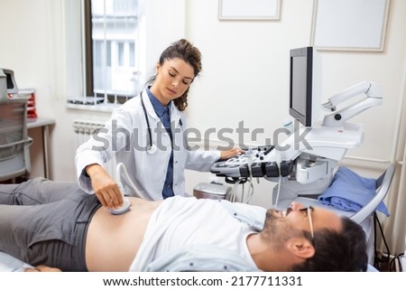 Young male patient lying on bed and having ultrasound examination of abdomen in medical clinic Royalty-Free Stock Photo #2177711331