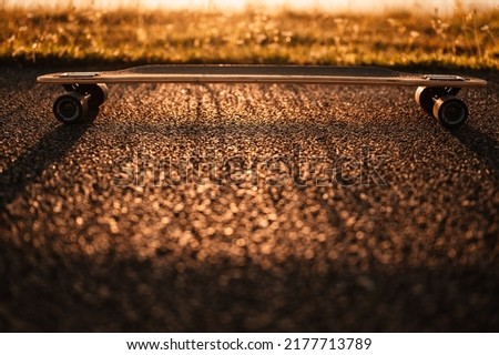 Woman rides at straight road on longboard at sunset time. Evening sunset with orange light. Longboard detail