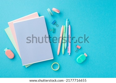 Back to school concept. Top view photo of colorful stationery stack of notebooks pineapple shaped erasers adhesive tape binder clips and pens on isolated blue background