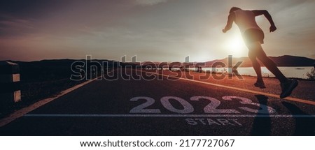 picture numbers 2023 written on the asphalt road and male runners are starting to run ready for new year at sunrise.Concept of challenge or career path and change.