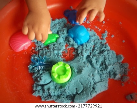 Defocused abstract background of hands of a kid playing with blue kinetic sand , close up