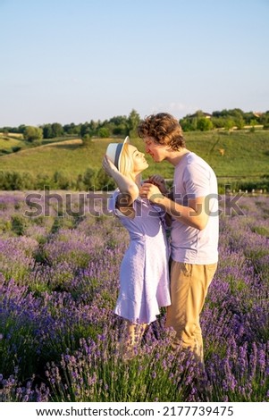 couple in purple lilac white outfit hugging, kissing in lavender field, photo session. man is holding woman in hands. Romance