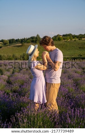 couple in purple lilac white outfit hugging, kissing in lavender field, photo session. man is holding woman in hands. Romance