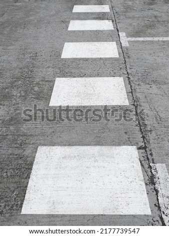 Perspective view of white crosswalk markings painted on the pavement. White discontinuous signage. Traffic signals.