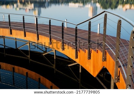 Pedestrian crossing over the water, wooden stairs with steps made of boards, a road circular bypass on the lake, a walking area on the pond, metal railings of the fence. High quality photo