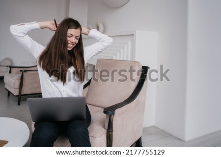Workaholic young dark haired pretty brunette woman stretching, sitting on chair with laptop eyes closed at home. Cheerful pretty Hispanic girl in white shirt needs break, overloaded remote working.