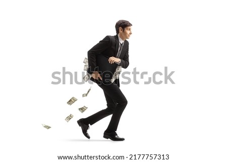 Full length profile shot of a businessman running and holding a briefcase full of money isolated on white background Royalty-Free Stock Photo #2177757313