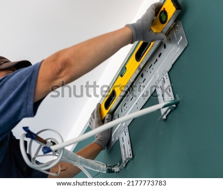 Male worker uses water level meter measuring wall when installing air conditioner. Man who fastens metal mount for air conditioner unit on inside wall of house. Selective focus. Royalty-Free Stock Photo #2177773783