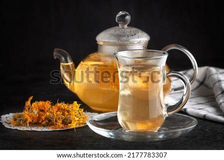 A teapot and a cup with healing tea. Dried marigold flowers.