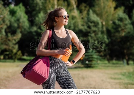 Slim fit woman walking with a big sports bag outdoors in the park
