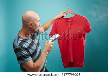 A man using vertical steamer for to iron red  t-shirt on blue background.