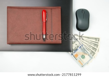 Dollar bills on a white background next to a laptop, notepad, red pen and computer mouse. Online business sale. Financial business success.