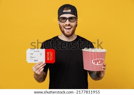 Young smiling happy cool cheerful satisfied man in 3d glasses watch movie film hold bucket of popcorn in cinema look camera isolated on plain yellow background studio portrait Tattoo translate fun.