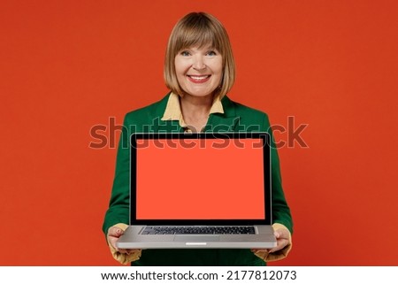 Elderly woman 50s in green classic suit hold use work on laptop pc computer with blank screen workspace area isolated on plain orange color background studio portrait People business lifestyle concept