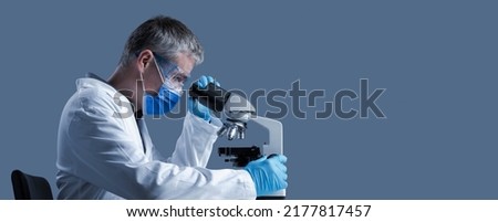 Scientist with face mask examining a sample under the microscope, scientific research concept, blank copy space Royalty-Free Stock Photo #2177817457
