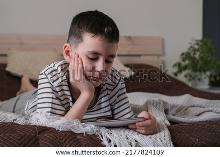 The boy lies on the bed and watches a cartoons and video on a smartphone