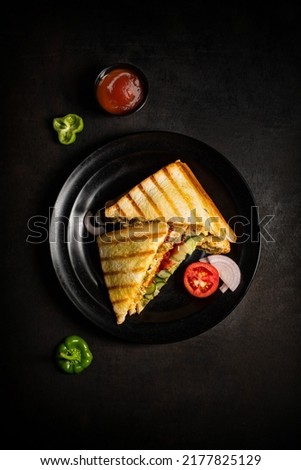 veg toast sandwich photography top angle shoot on grey-black texture background and garnish in black a plate with tomato ketchup in a bowl and some raw tomato capsicum, onion, and mint leaves.    Royalty-Free Stock Photo #2177825129