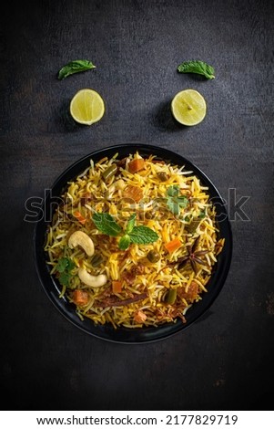 veg biryani tabletop photography styled on black-grey texture background garnished in black a bowl with fresh ingredients like mints leaves, lemon, and star anise. copy space is for the matter.