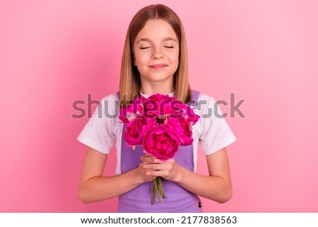 Photo of adorable little girl receive small present smell beautiful scent of peony isolated on pink color background