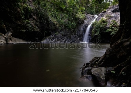Waterfall in deep forest in Saraburi, Thailand. rocks and tree roots in foreground. Long-exposure image.