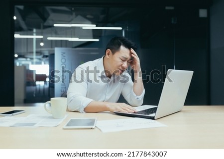 Businessman desperation, asian man working in office, looking at laptop screen, screaming in grief, got bad news Royalty-Free Stock Photo #2177843007