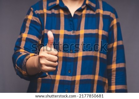 A businessman in a blue shirt shows thumbs up while standing on gray background in the office. Customer service and satisfaction surveys concept. Close-up photo